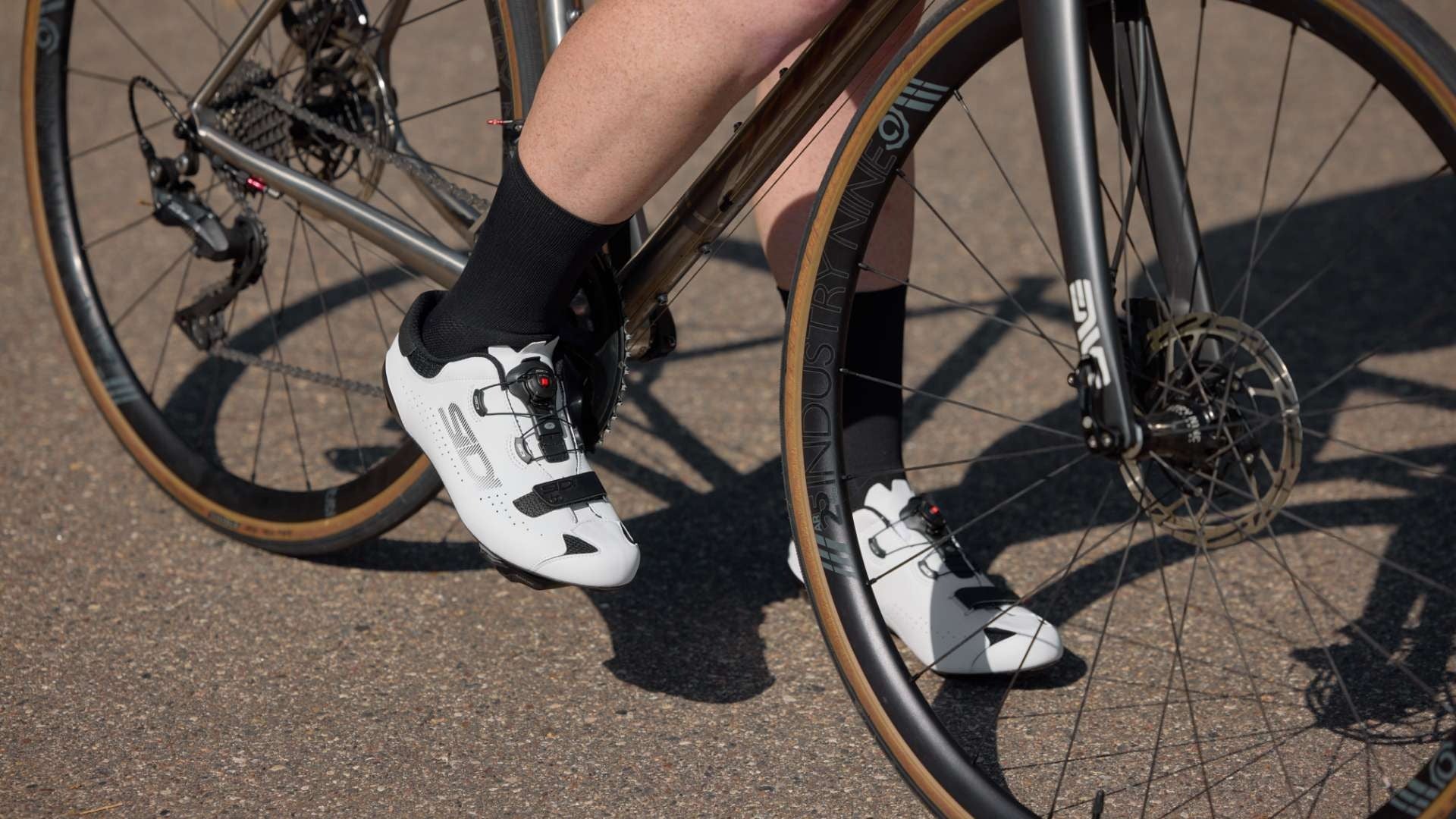 Person wearing white cycling shoes and black socks on a bicycle.
