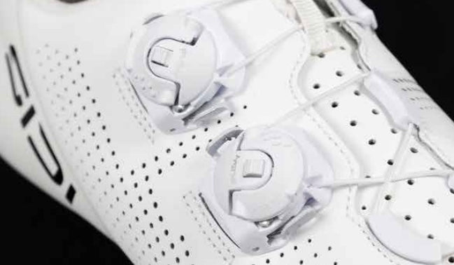 Close-up of a white sneaker and white dial system closure with brand logo on a black background