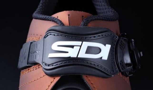 Brown leather boot with a black Sidi brand instep closure strap on a dark background